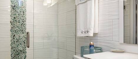 A bathroom with a glass shower enclosure, a white toilet, and a vanity with a mirror.