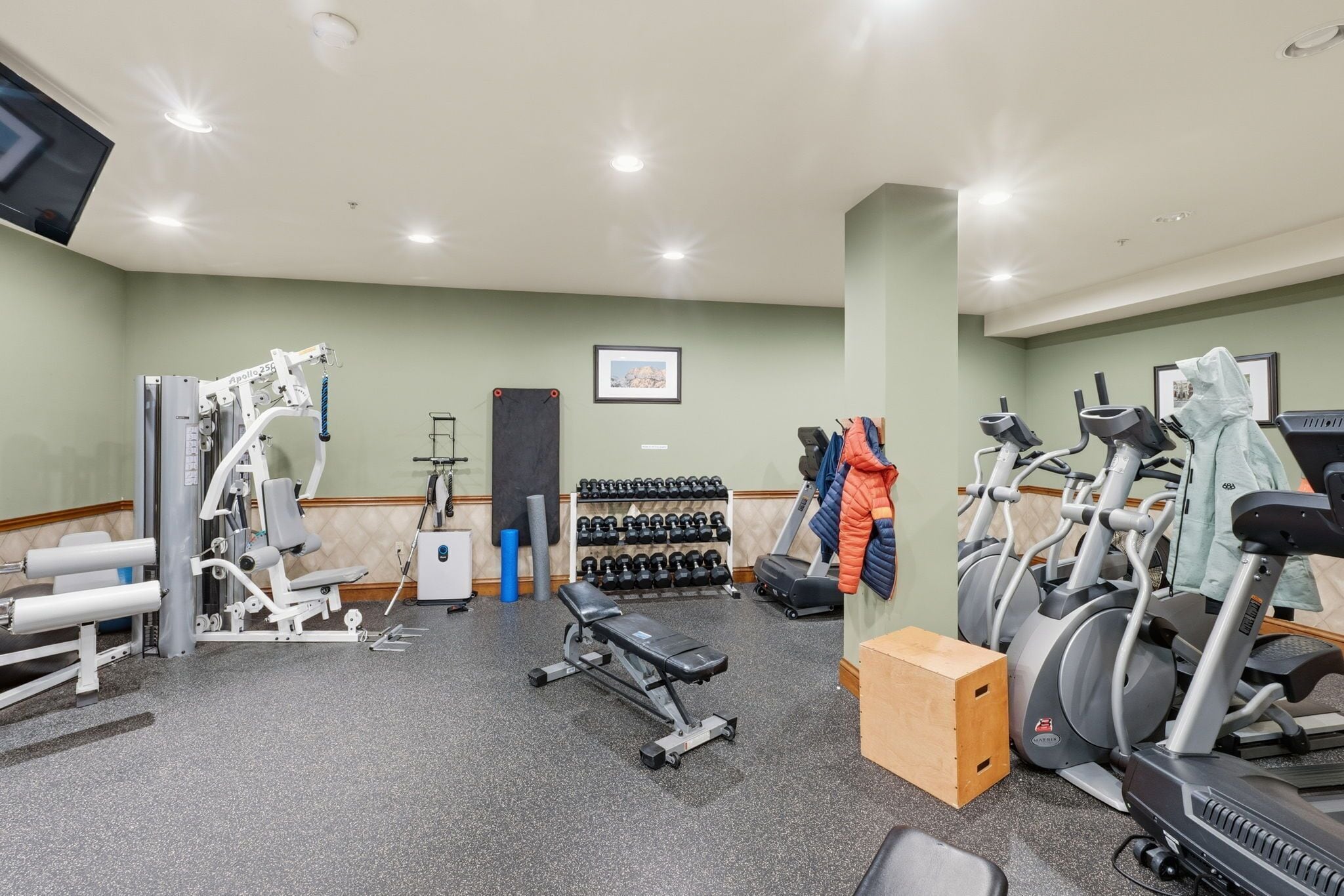 Un gimnasio con equipo de ejercicio, una banca, mancuernas y un televisor.