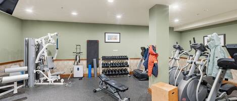 Ett gym med träningsutrustning, en bänk, hantlar och en tv.