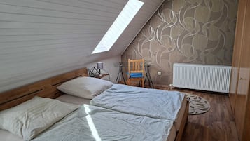 Ein Schlafzimmer mit schrägem Dach, einer Dachfensterkuppel, einem Bett mit zwei Kissen, einem Sessel und einer Heizung.