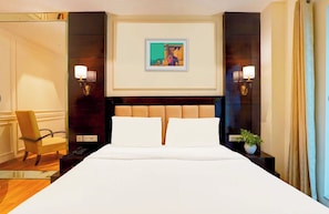 A hotel room with a large bed, two bedside lamps, a framed picture on the wall, a chair, and a potted plant. - Imperial Villa By Hotel GreySky NewDelhi (New Delhi)