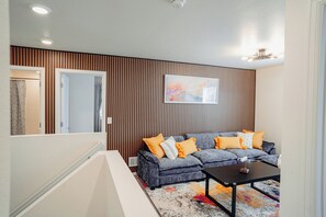 Un salon moderne avec un canapé gris, des coussins orange, une table basse et un tapis coloré.