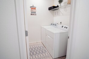 Une buanderie avec un lave-linge et un sèche-linge blancs, un étendoir et un panneau indiquant les instructions de lavage.