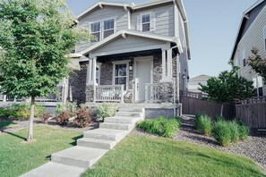 A two-story residential house with a front porch, stone foundation, and a small front yard with steps leading to the entrance. - Stylish 3BR Home + Office - Minutes from DIA & Gaylord (Aurora)