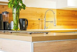 Eine Küche mit Holztischplatte, einem Mixer, einer Kaffeemaschine und einer Vase mit grünen Blättern.