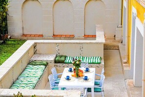 Eine Terrassengruppe im Freien mit Tisch für zwei Personen, gepolsterten Sitzmöglichkeiten und einer dekorativen Vase.