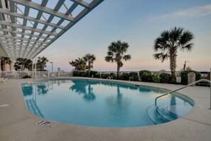 A swimming pool with a white deck, surrounded by palm trees and a white fence. - Beautifully remodeled, oceanfront condo + Free Attraction Tickets! (North Myrtle Beach)