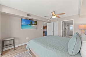 A bedroom with a bed, a ceiling fan, a TV, and a view of a kitchen and bathroom. - Beautifully remodeled, oceanfront condo + Free Attraction Tickets! (North Myrtle Beach)