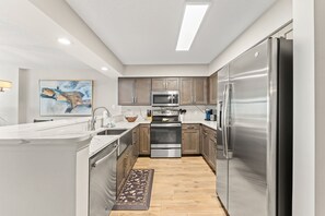 A modern kitchen with stainless steel appliances, wooden cabinets, and a marble countertop. - Beautifully remodeled, oceanfront condo + Free Attraction Tickets! (North Myrtle Beach)