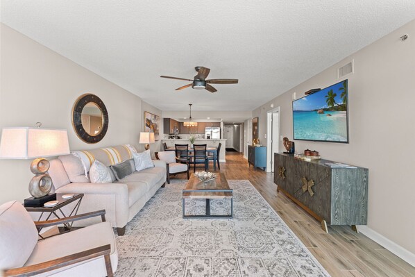 A modern living room with a sofa, coffee table, and a dining area with chairs. - Beautifully remodeled, oceanfront condo + Free Attraction Tickets! (North Myrtle Beach)