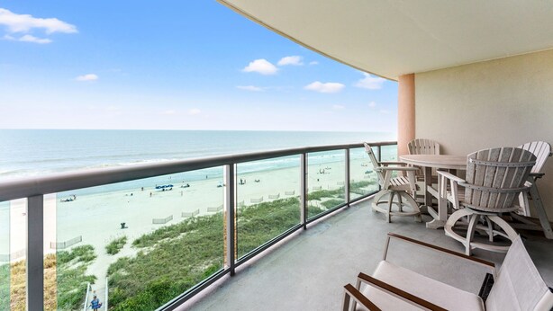 Uma varanda com vista para a praia, uma mesa e duas cadeiras.
