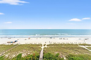 Ein Strand mit einer Holzpromenade, die zum Ufer führt, feinem Sand und dem Meer.