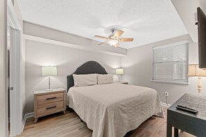 A bedroom with a bed, two bedside tables with lamps, a ceiling fan, and a window with blinds. - Beautifully remodeled, oceanfront condo + Free Attraction Tickets! (North Myrtle Beach)