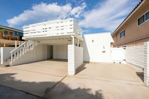A building with a covered parking area, a staircase leading to an upper level, and a number '1945' visible on the structure. - Casa Del Mar - Designer Home, 1 Block to Beach (Del Mar)