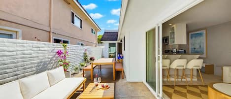 A modern apartment with a patio area, a dining table, and a kitchen visible through the sliding glass door.