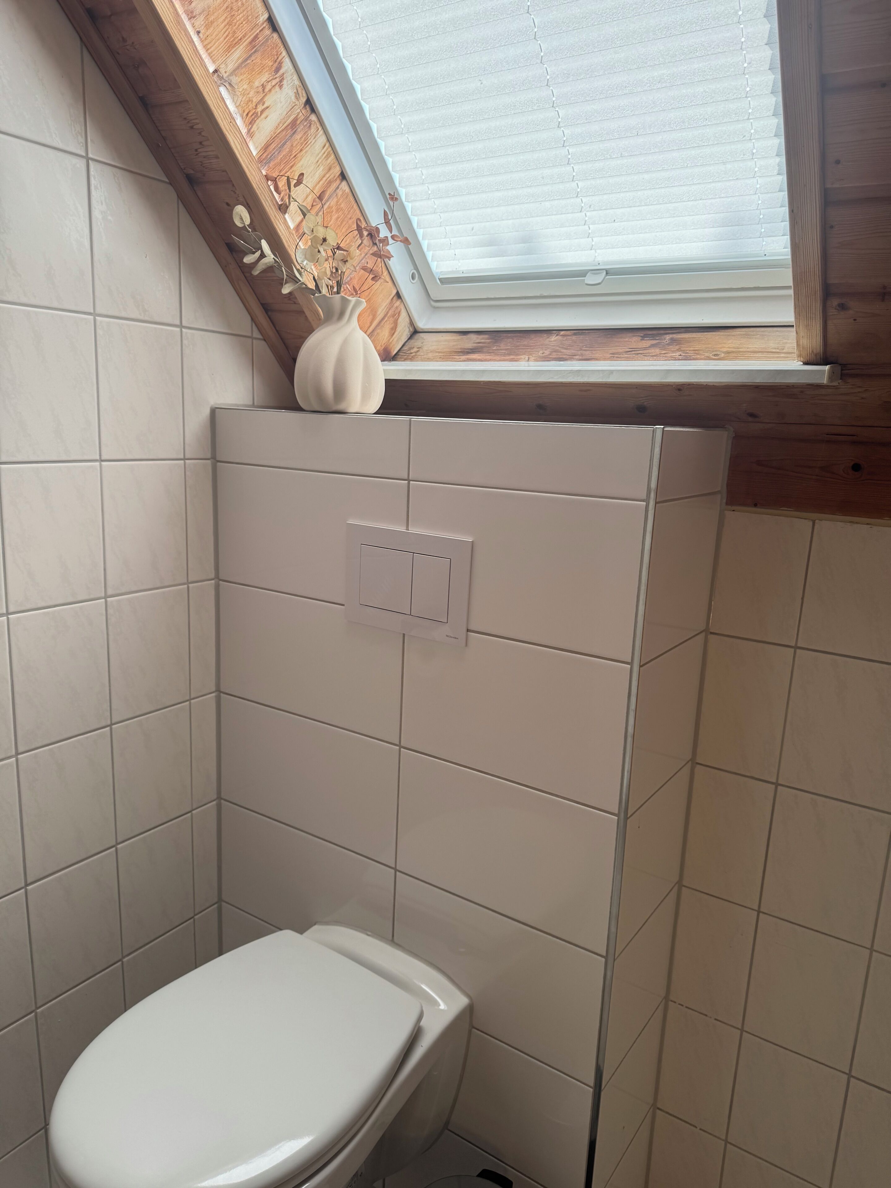 Un baño pequeño con azulejos, un inodoro, un interruptor de luz y una ventana con persianas.