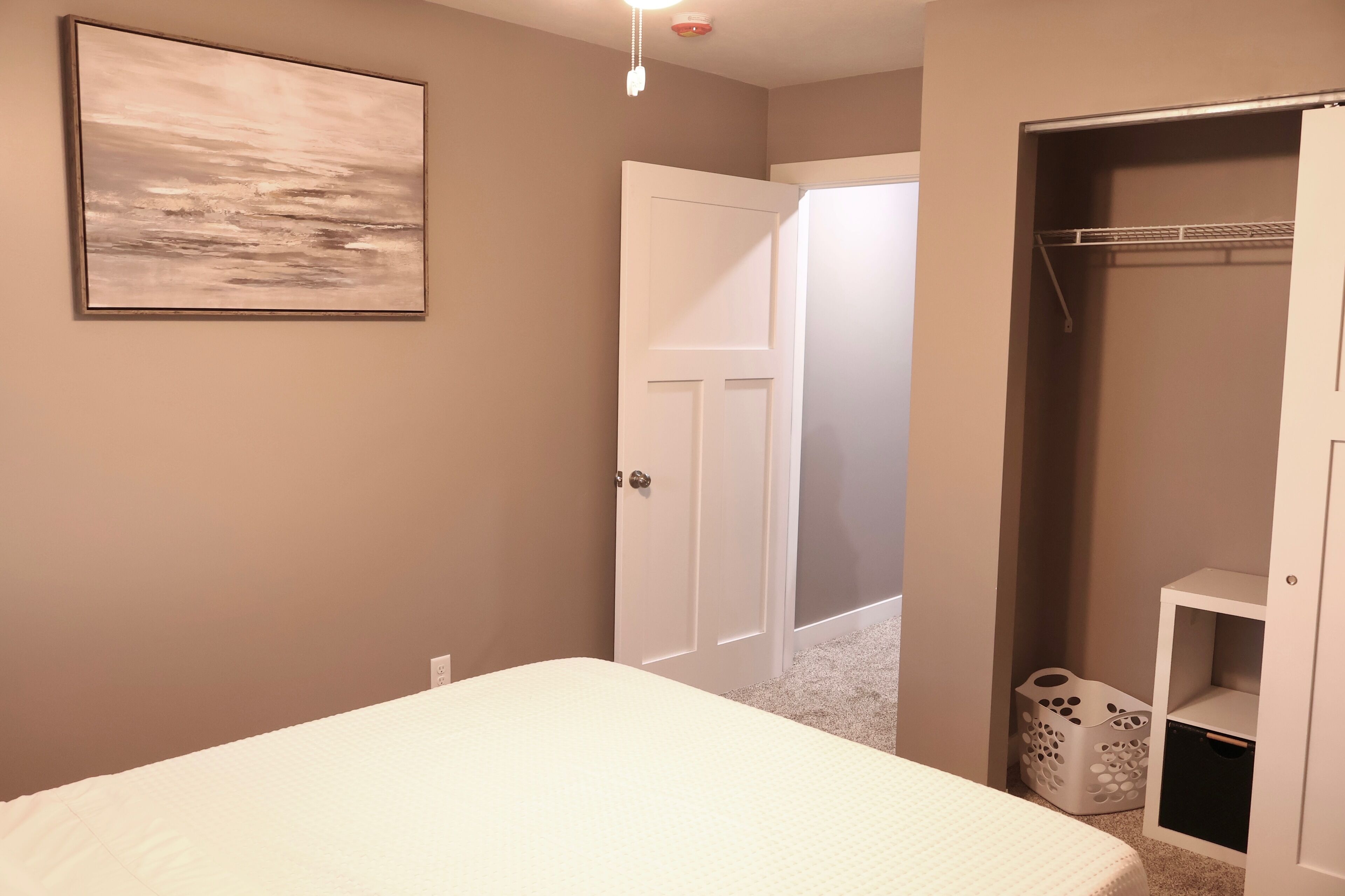 Un dormitorio con una cama, un armario con estantes y una puerta que da a otra habitación.