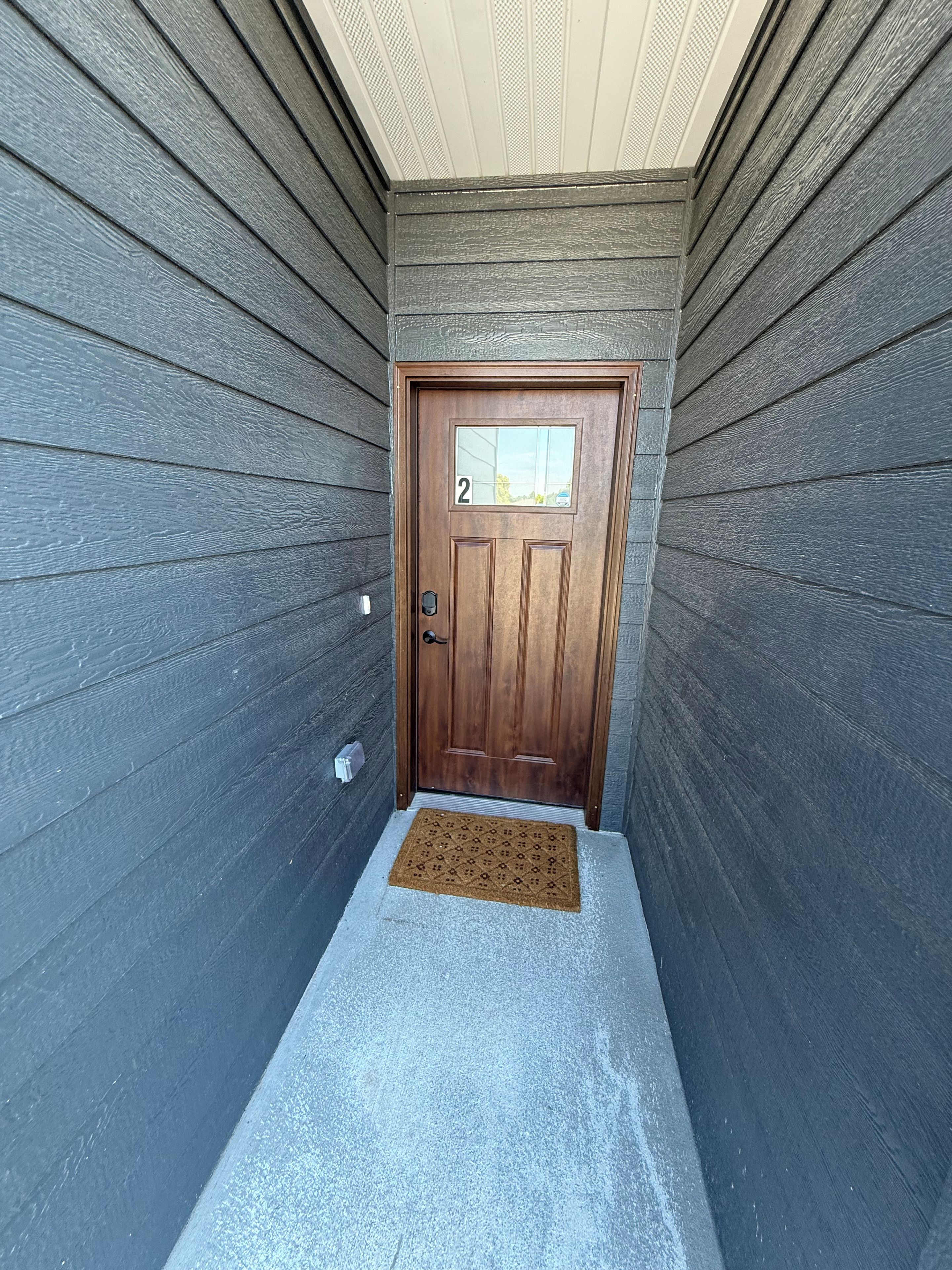 Una puerta de madera con un letrero con el número '2', un felpudo y un escalón pequeño que lleva a la entrada.
