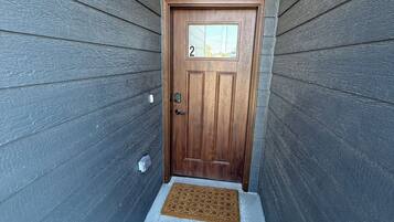 Una puerta de madera con un letrero con el número '2', un felpudo y un escalón pequeño que lleva a la entrada.