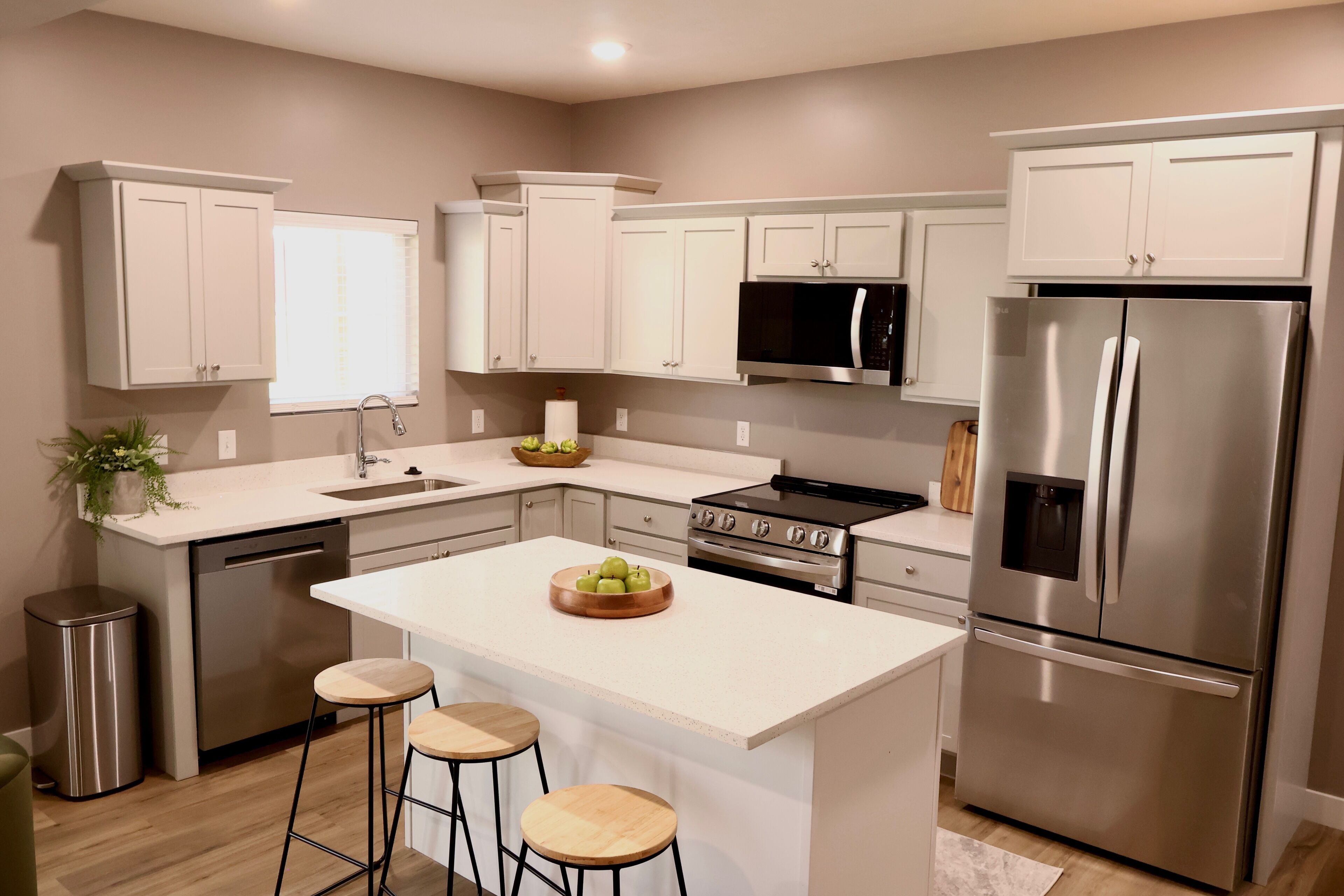 A modern kitchen with white cabinetry, stainless steel appliances, and a central island with stools.