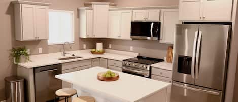 A modern kitchen with white cabinetry, stainless steel appliances, and a central island with stools.