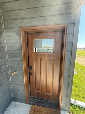 A wooden door with a glass panel and a number '1' sign, a brass door knocker, and a doormat.