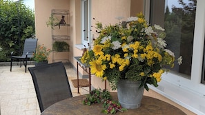 Un patio con una mesa, sillas, una maceta con flores amarillas y una escultura de metal.