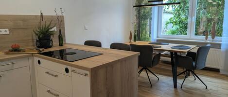 Una cucina moderna con isola centrale, zona pranzo con sedie e vista su piante.