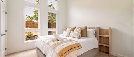 A bedroom with a large bed, two windows, a wooden headboard, and a built-in shelf.