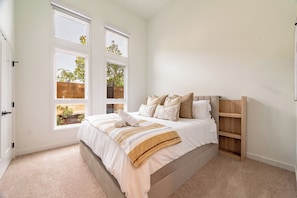 A bedroom with a large bed, two windows, a wooden headboard, and a built-in shelf.