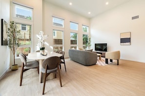A modern living room with a dining area, large windows, and a flat-screen TV.