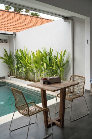 Un área de estar al aire libre con piscina, rodeada de vegetación y un techo de tejas.