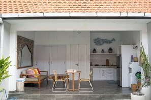Un espace extérieur abrité comprenant une table et des chaises, un canapé, un coin cuisine avec des placards et un réfrigérateur, ainsi qu’un élément décoratif mural.