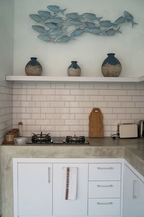 Une cuisine avec des meubles blancs, une cuisinière à gaz, un grille-pain et, au-dessus des meubles, une décoration murale représentant des poissons.