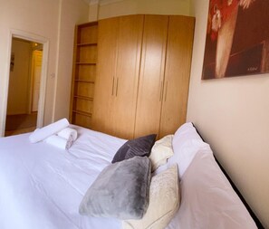 Un dormitorio con cama, almohadas, un armario de madera y un cuadro en la pared.