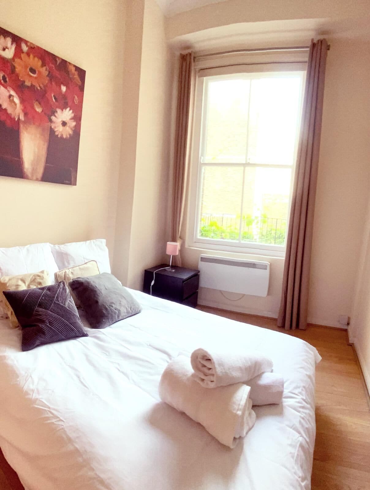 A neatly made bed with pillows and a rolled towel, a bedside table with a lamp, and a window with curtains.