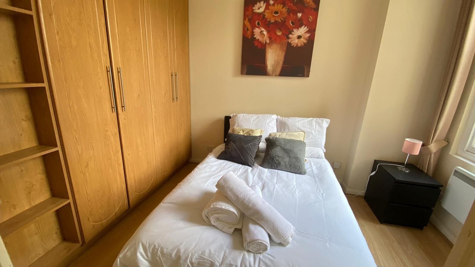 Une chambre à coucher avec un lit, des oreillers, une table de chevet avec une lampe, une armoire en bois et un tableau au mur.