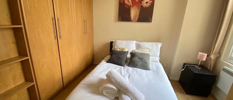 Une chambre à coucher avec un lit, des oreillers, une table de chevet avec une lampe, une armoire en bois et un tableau au mur.
