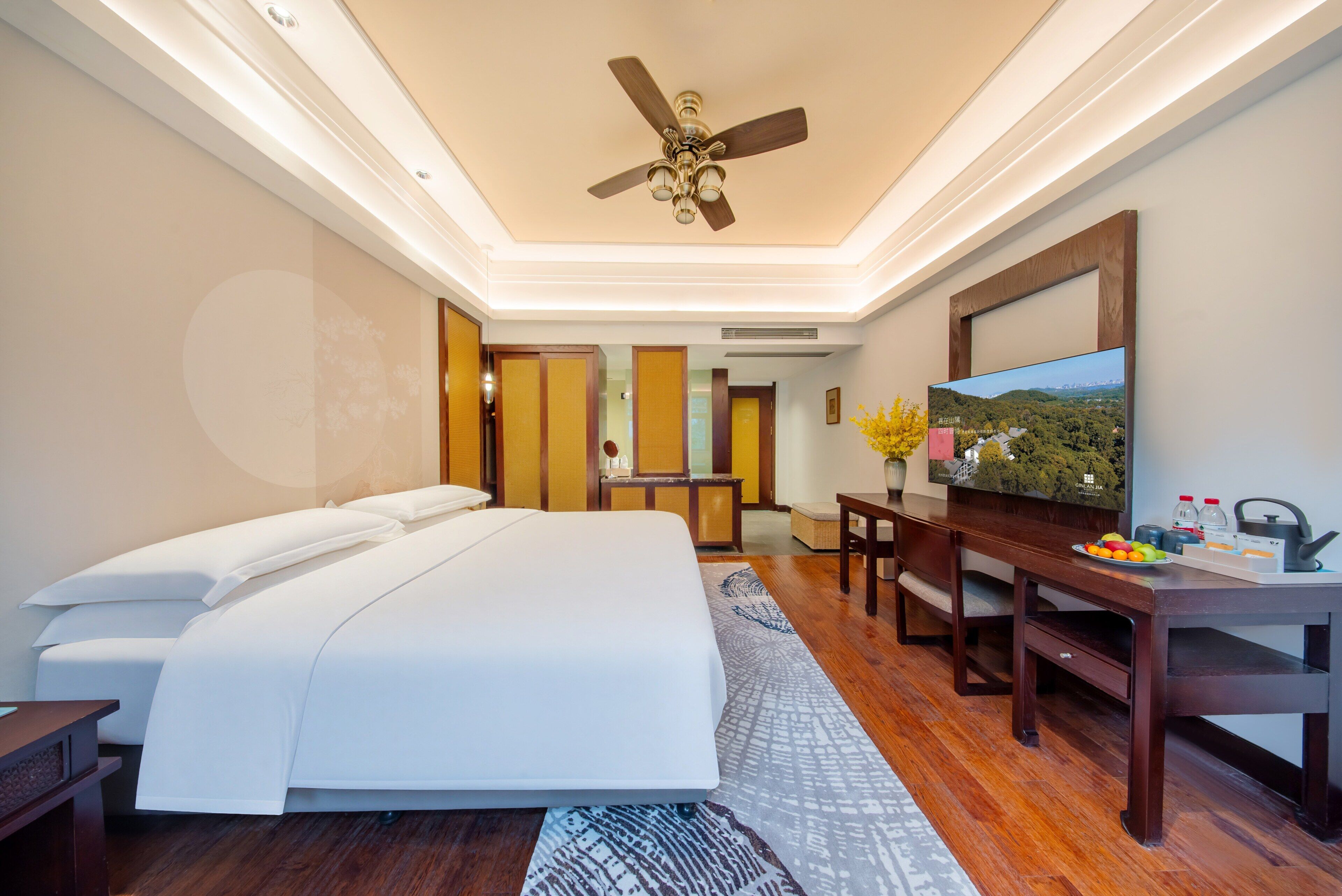 Habitación de hotel con cama, escritorio, televisor y ventilador de techo.