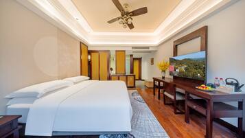 Habitación de hotel con cama, escritorio, televisor y ventilador de techo.