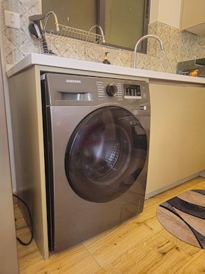 Una lavatrice a carica frontale Samsung in una cucina con zoccolo a mosaico e pavimento in legno.