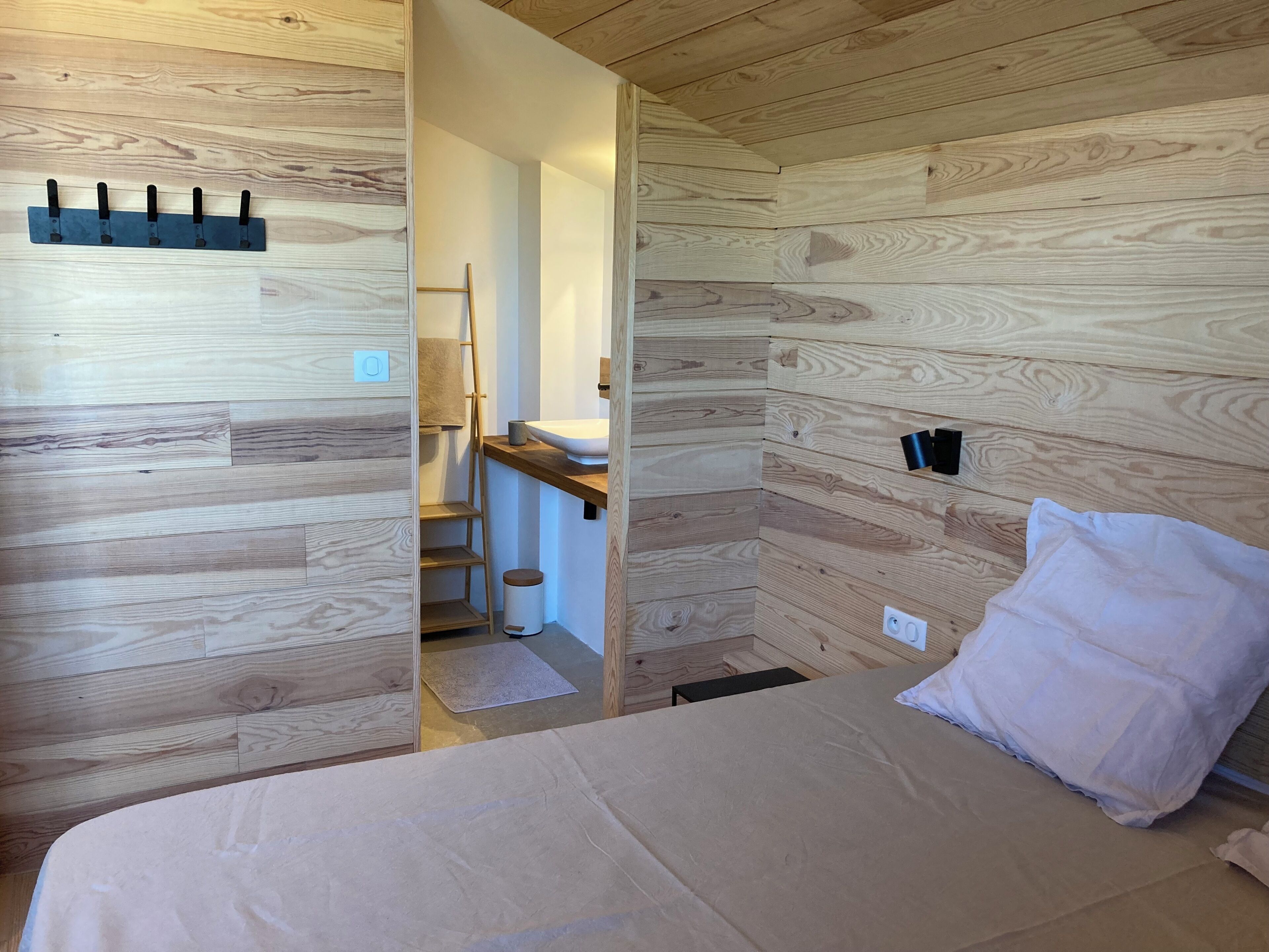 Ein Zimmer mit einem Bett, einer Holzwand, einem Waschbecken und einer Leiter.