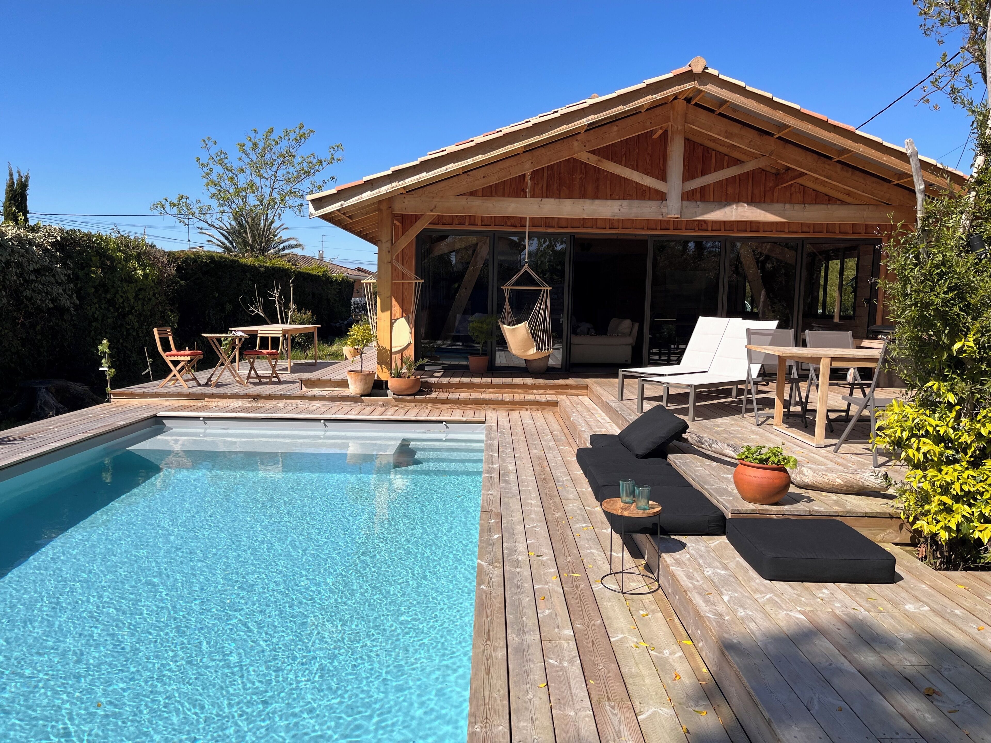 Une terrasse en bois avec une piscine, du mobilier d’extérieur et un espace salon abrité.