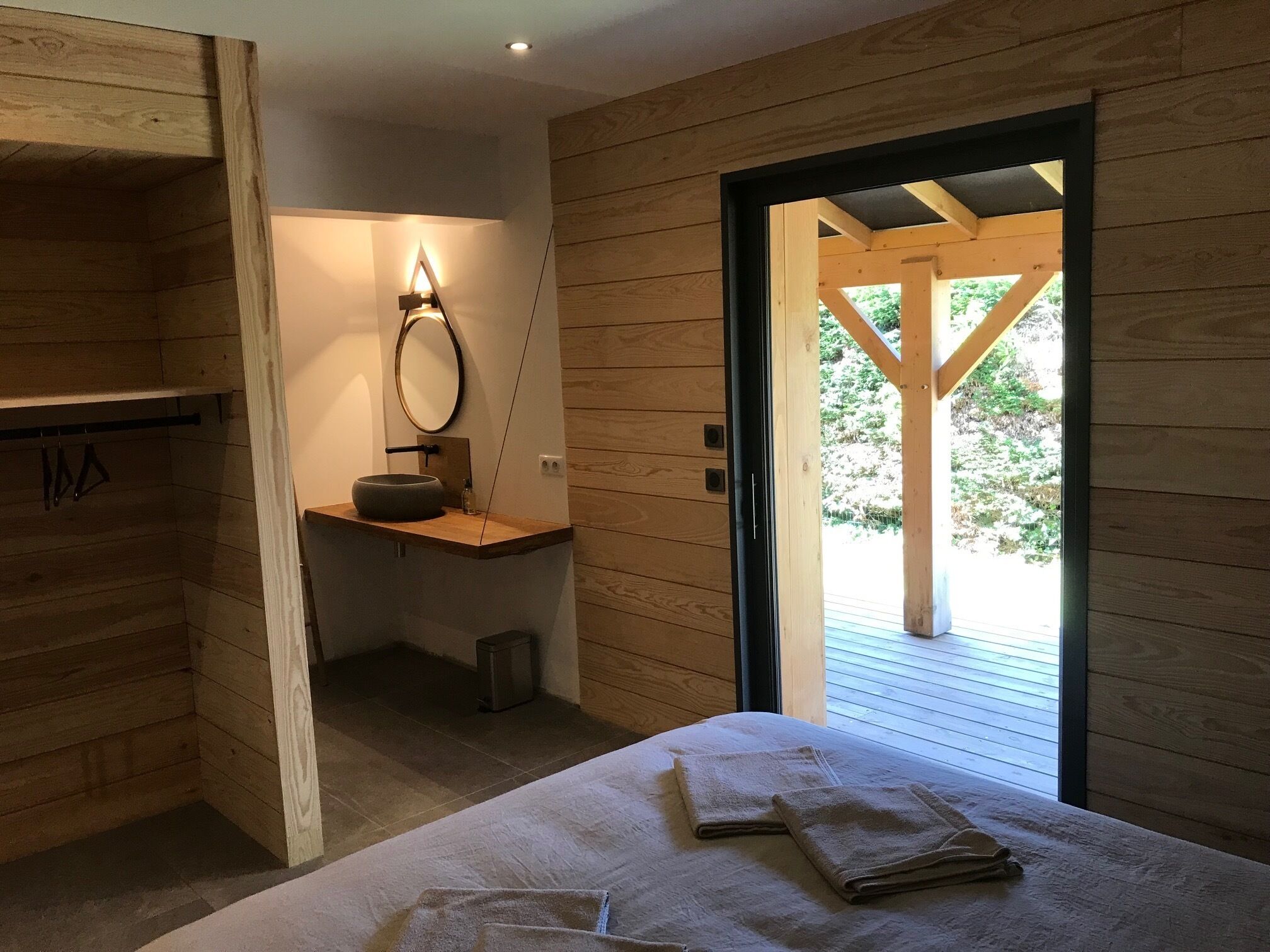 Een houten interieur met een bed, een kleine badkamer en uitzicht door een open deur.