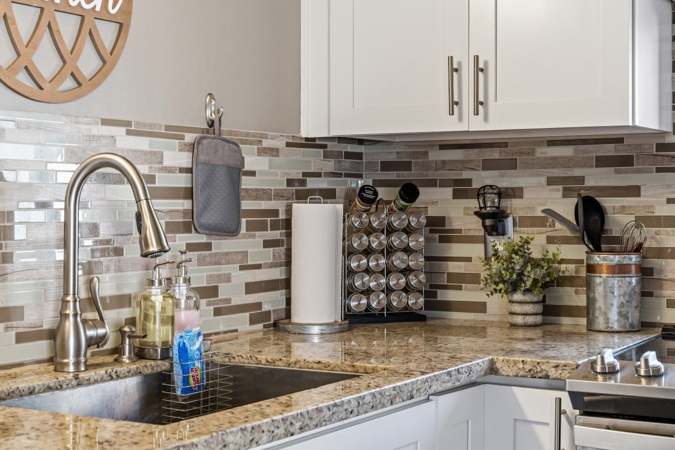 A kitchen with a granite countertop, stainless steel faucet, a hanging pot rack, and a spice rack.