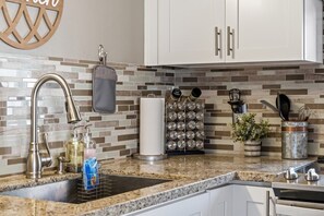 Una cocina con encimera de granito, grifo de acero inoxidable, un colgador para ollas y un especiero.