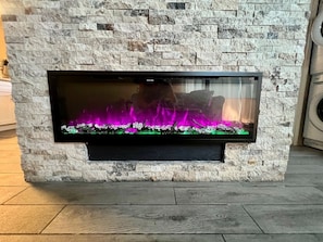 Una llar de foc amb un fons de pared de pedra, un televisor de pantalla plana penjat a la part superior i un paviment de fusta.