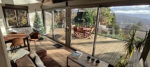 Un interior moderno con terraza de madera, zona de comedor y un amplio ventanal con vistas panorámicas.