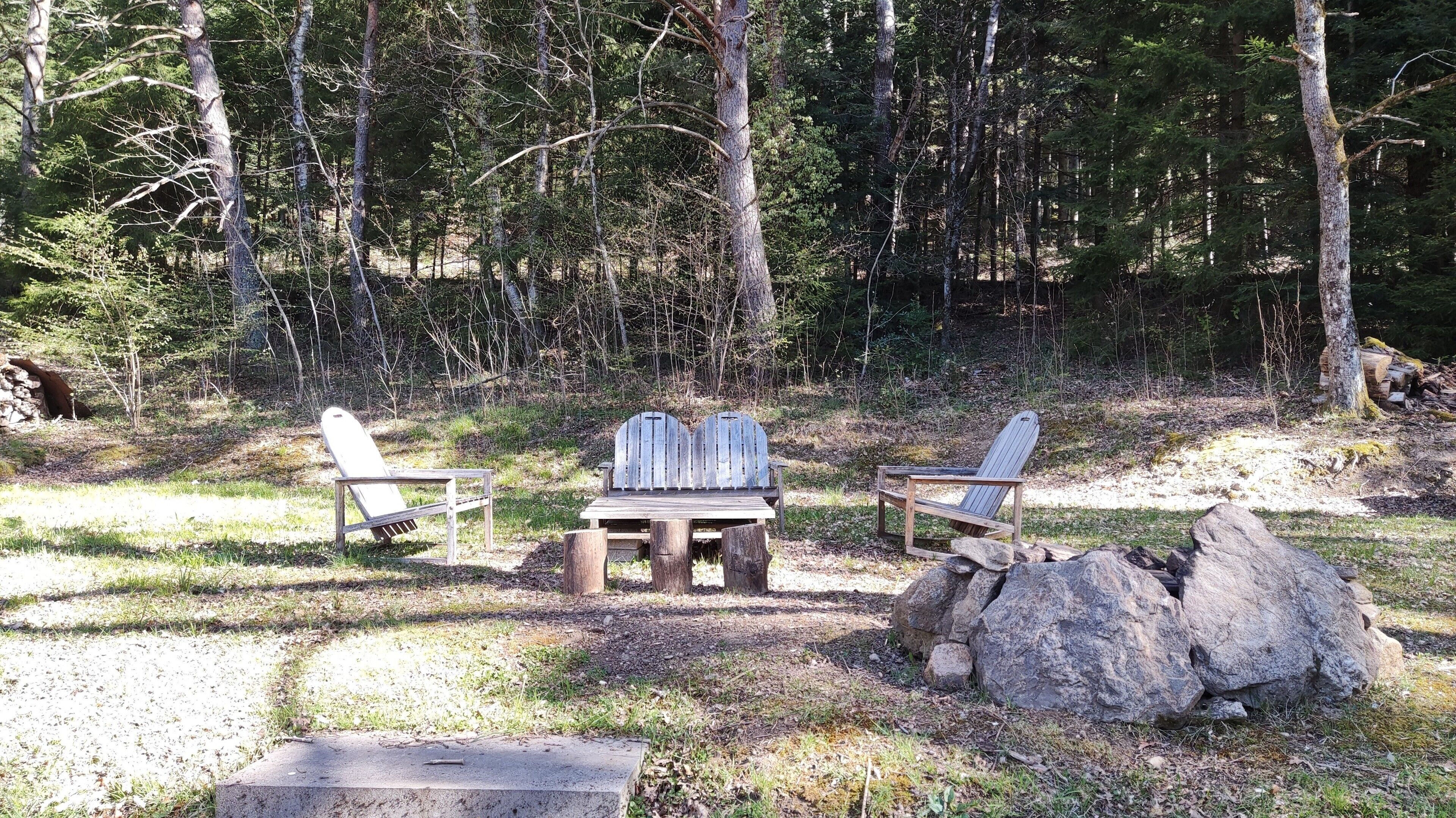 En campingplats med två Adirondack-stolar, ett träbord och en stor sten.