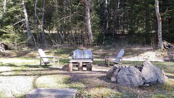 En campingplats med två Adirondack-stolar, ett träbord och en stor sten.